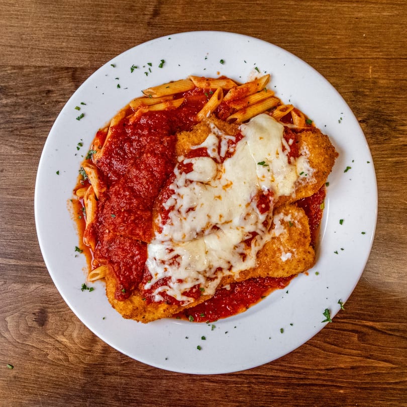Pesto's chicken parmesan with penne pasta, marinara sauce, and melted mozzarella on a white plate.