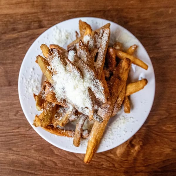 A white plate filled with golden-brown french fries, generously topped with grated Parmesan cheese.