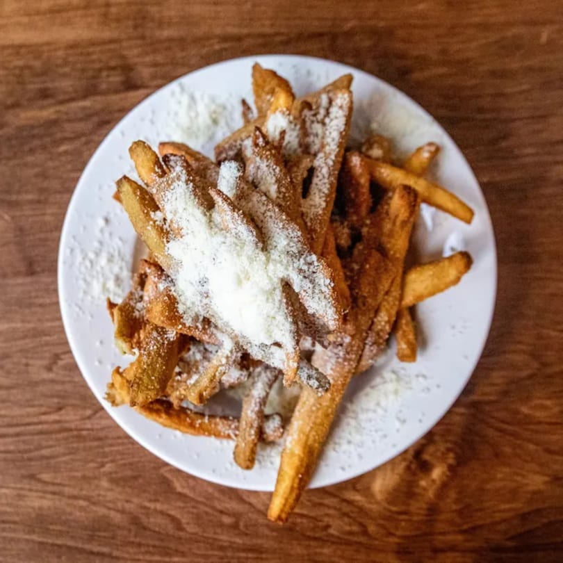 A white plate filled with golden-brown french fries, generously topped with grated Parmesan cheese.