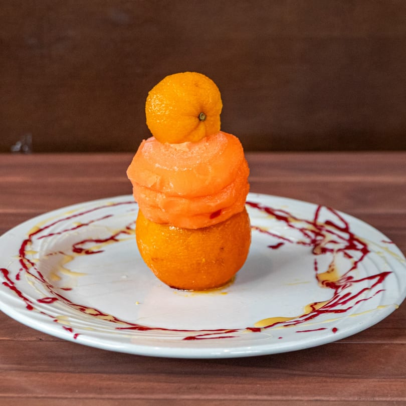 A tower of orange sorbet and citrus fruit on a white plate with red and yellow sauce.