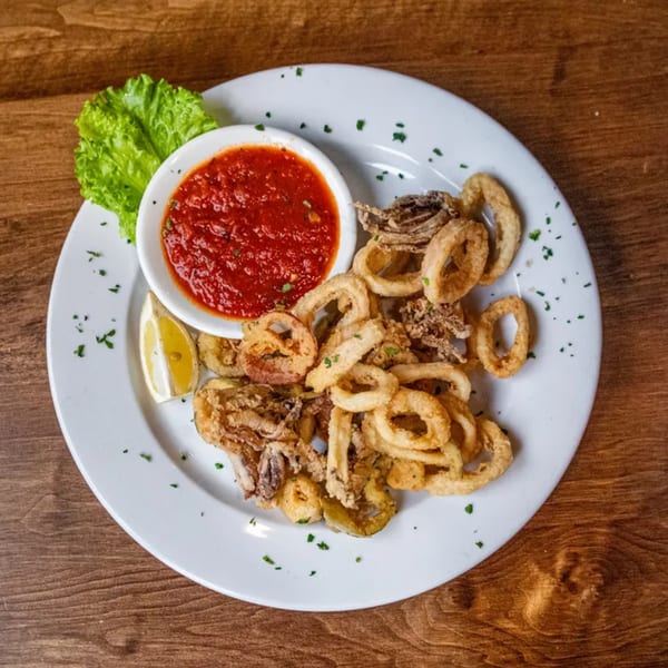 Crispy fried calamari and vegetables with a side of red marinara sauce, lemon, and lettuce.